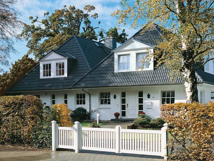 Elegantes zweigeschossiges Haus mit Satteldach, umgeben von Garten und weißem Zaun. Großer Eingangsbereich sichtbar.