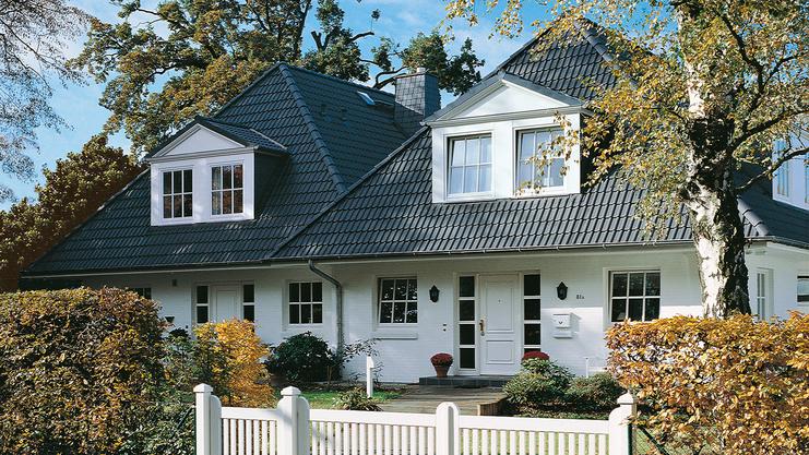 Elegantes zweigeschossiges Haus mit Satteldach, umgeben von Garten und weißem Zaun. Großer Eingangsbereich sichtbar.